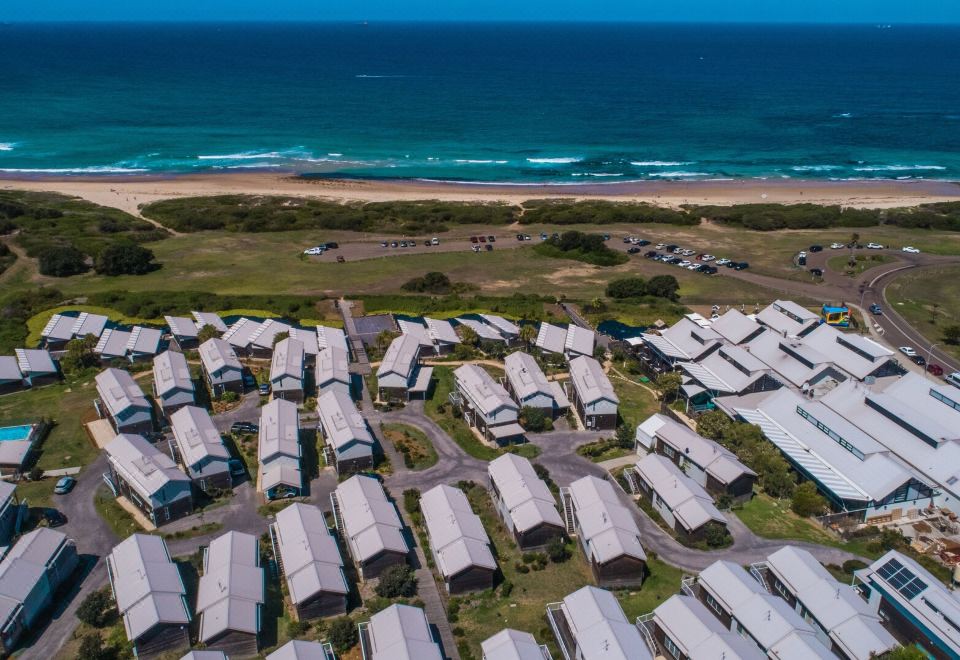 a large group of white houses are scattered across a beach with the ocean in the background at Caves Coastal Bar & Bungalows