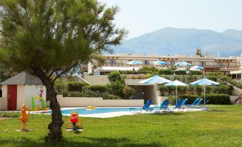 a swimming pool surrounded by grass , with several lounge chairs and umbrellas placed around it at Grecotel Meli Palace