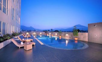 a rooftop pool area with multiple lounge chairs and a swimming pool , surrounded by a building with a mountainous view at Atria Hotel Malang