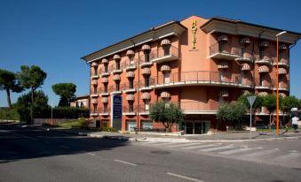 a brick building with multiple floors , surrounded by trees and a street with cars parked on the side at Best Western Cesena Hotel