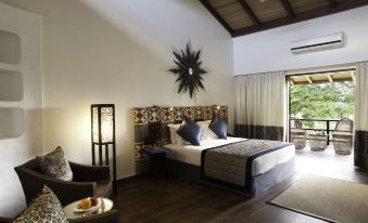 a large bed with a decorative headboard is in a room with a chair and a table at The Serai Bandipur