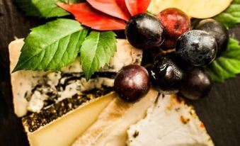 a black wooden cutting board filled with various types of cheese and grapes , accompanied by a leafy leaf at Bayerischer Hof