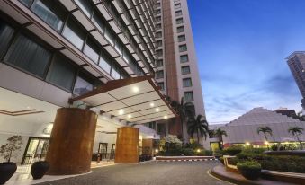 a modern building with a large glass facade and wooden pillars , set against a clear blue sky at Ascott Jakarta