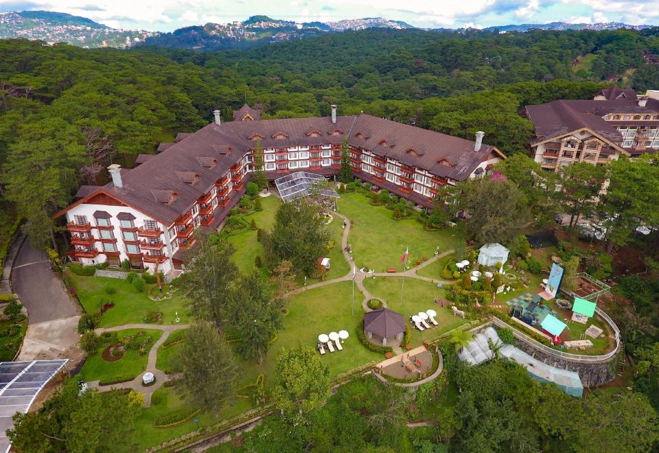 aerial view of a large hotel surrounded by trees and mountains , with a swimming pool visible in the courtyard at The Manor at Camp John Hay