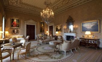 a luxurious living room with high ceilings , ornate furniture , and chandeliers , including a large painting on the wall at Ballyfin Demesne