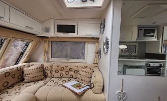 a cozy living room in a motorhome , with a couch , tv , and coffee table , as well as a window with sunlight coming in at Glamping with Llamas