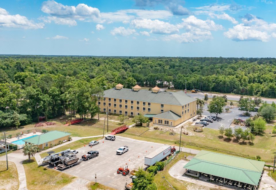 a large , multi - story building with a green roof is surrounded by trees and parking lots at Magnuson Hotel Wildwood Inn Crawfordville