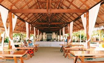 a large , open - air wooden structure with thatched roofs , containing several tables and chairs for dining at La Luz Beach Resort