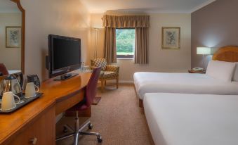 a hotel room with two beds , a desk , and a tv , along with a window and chair at Delta Hotels Milton Keynes