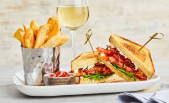 a plate of food , including a sandwich , fries , and a glass of wine , placed on a dining table at Courtyard Troy