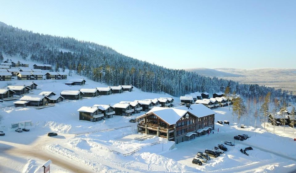 a snow - covered village with houses and cars parked in the snow , set against a clear blue sky at Mountain Lodge