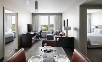 a modern living room and dining area with a large window , red leather chairs , and white plates on the table at Residence Inn by Marriott Boston Watertown