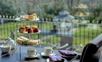 a three - tiered cake stand filled with pastries and sandwiches , placed on a table in a room at Burnley West Higher Trapp Hotel