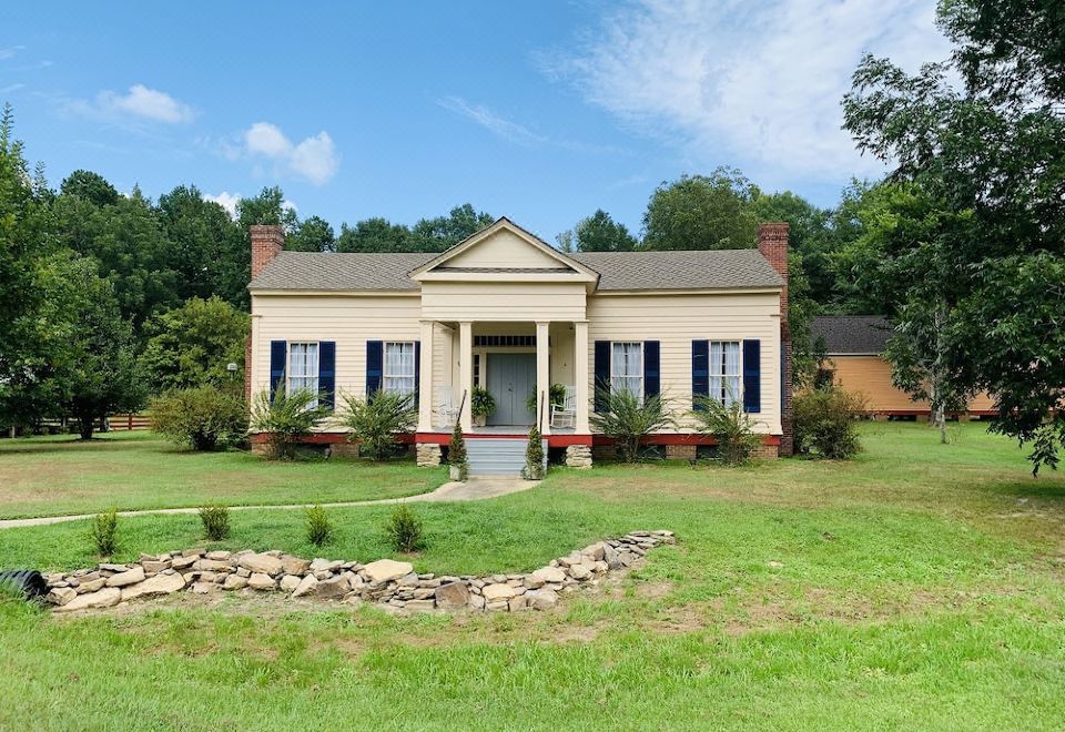 a large white house with blue shutters , surrounded by green grass and trees , under a clear blue sky at Coulter Farmstead