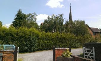 a gravel driveway leading up to a house with a church in the background , surrounded by trees at Church Farm Accommodation