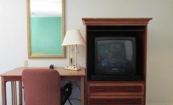 a small room with a television on top of a wooden cabinet , a desk , and a chair at Village Inn