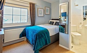 a cozy bedroom with a blue bedspread , white curtains , and a window , along with a bathroom door visible at The Pytchley Inn