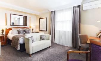 a well - decorated hotel room with a white couch , bed , and chair , along with a window and curtains at Brandshatch Place & Spa