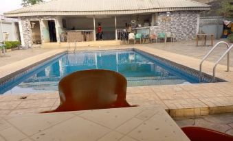 a swimming pool with a white tiled base and wooden tables , chairs , and umbrellas in the foreground at Brentwood Hotel