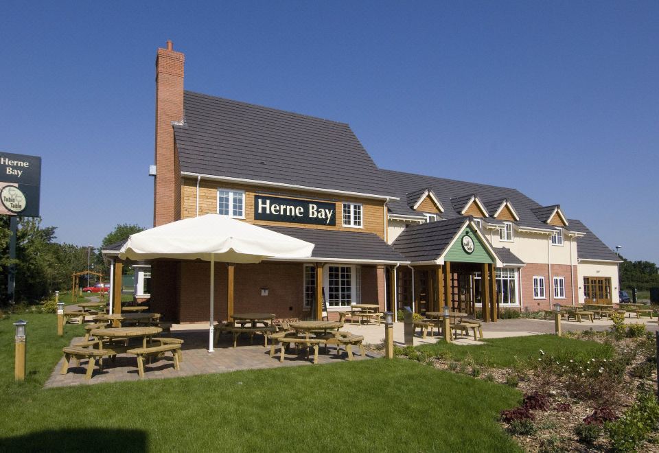 "a brick building with a sign that says "" herne bay "" is surrounded by green grass and a picnic area" at Premier Inn Herne Bay