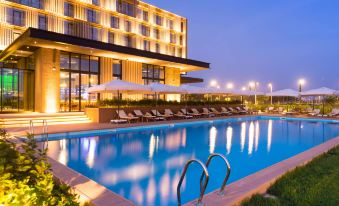 a large swimming pool with a pool chairs and umbrellas in front of a modern hotel at Radisson Hotel, Dakar Diamniadio