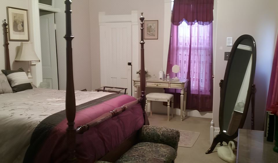 a room with a bed , a desk , and a chair , all decorated in white and purple at Smithville Historical Museum and Inn