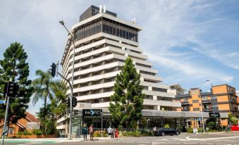 a tall white building with a curved roof and many windows , situated in the middle of a city street at Mercure Brisbane Spring Hill