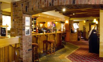 a well - lit bar with wooden furniture , including a counter and stools , surrounded by brick walls and a carpeted floor at Premier Inn Pontefract North