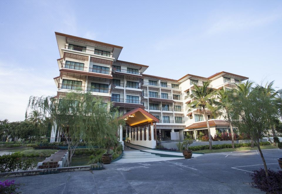 a large , modern building with multiple balconies and a sign above the entrance , surrounded by trees and a parking lot at RK Riverside Resort & Spa (Reon Kruewal)