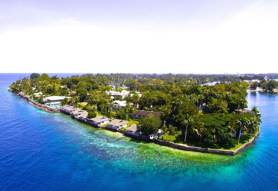 a scenic view of a tropical island with clear blue water , lush green trees , and white buildings at Madang Resort