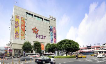 a busy city street with numerous cars , trucks , and motorcycles driving by a large shopping mall at Le Room Hotel Taoyuan