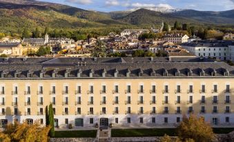 a large white building with many windows is situated in the middle of a city with mountains in the background at Parador de La Granja