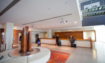 a hotel lobby with a reception desk , a couple of people standing near it , and an orange carpet at PARKROYAL Melbourne Airport