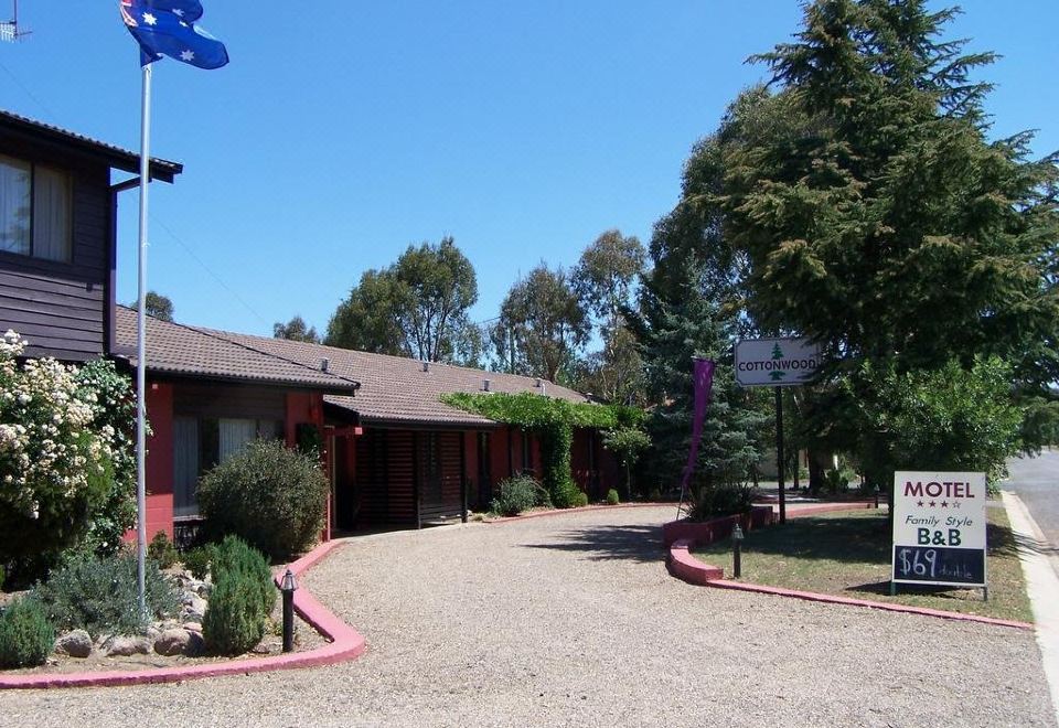 a brick building with a red roof , situated next to a dirt road and surrounded by trees at Cottonwood Lodge