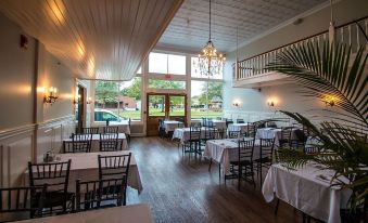 a large dining room with wooden floors , white tablecloths , and black chairs arranged around tables at Meadows Hotel