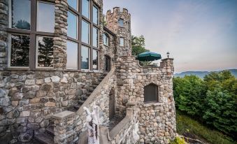 a castle - like building with a stone staircase leading up to it , surrounded by trees and overlooking a body of water at Highlands Castle Overlooking Lake George Plus 2 Other Castles & Suites