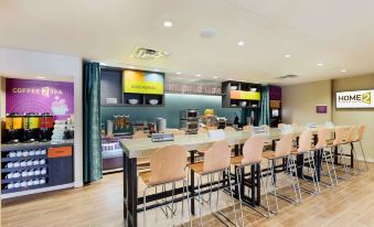 a dining area with several tables and chairs , as well as a tv mounted on the wall at Home2 Suites by Hilton Omaha/West