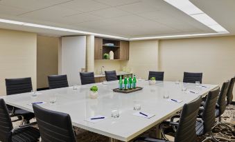 a conference room with a long white table surrounded by black chairs and green bottles on the table at Delta Hotels Chicago Willowbrook