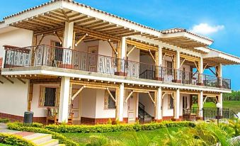 a large white house with a balcony and multiple balconies is surrounded by green grass and flowers at Hotel Campestre las Camelias