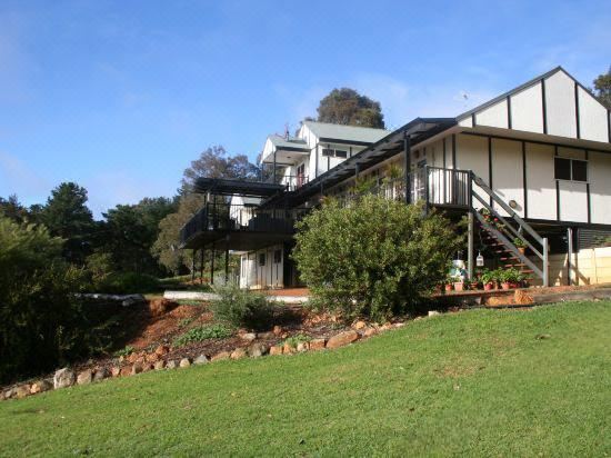 a large house with a balcony and stairs is surrounded by greenery on a hillside at Nannup Hideaway