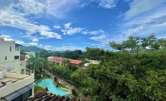 a view of a pool and buildings from a high vantage point , with blue skies and trees in the background at Tropical Gardens