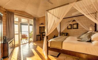 a bedroom with a canopy bed and large windows overlooking the ocean , creating a serene and peaceful atmosphere at Komandoo Island Resort & Spa