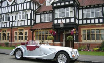 a silver vintage car parked in front of a red and white house , surrounded by trees at Colwall Park - Hotel, Bar & Restaurant