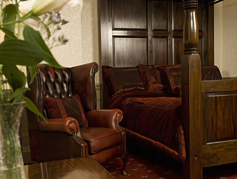 a cozy bedroom with a large bed , a leather chair , and a potted plant in the corner at The Old Lodge