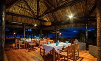 a wooden restaurant with tables and chairs under a thatched roof , overlooking the ocean at night at Nanuya Island Resort