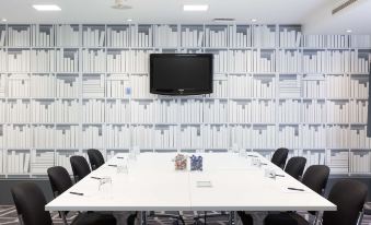 a conference room with a white table , black chairs , and a television mounted on the wall at Village Hotel Cardiff