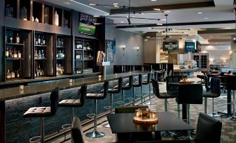 a modern restaurant with black chairs and tables , a bar , and a tv on the wall at Atlanta Marriott Alpharetta