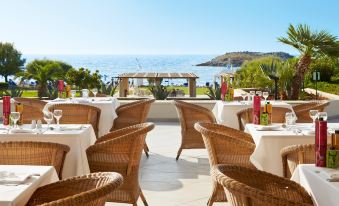 an outdoor dining area with tables and chairs arranged for a group of people to enjoy the view of the ocean at Grecotel Meli Palace