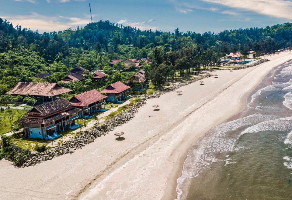 a picturesque beach resort with white sand and clear blue water , surrounded by lush green trees and buildings at Quynh Vien Resort Ha Tinh