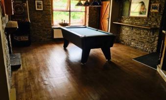 a pool table is set up in a room with wooden flooring and stone walls at The Gwaelod y Garth Inn